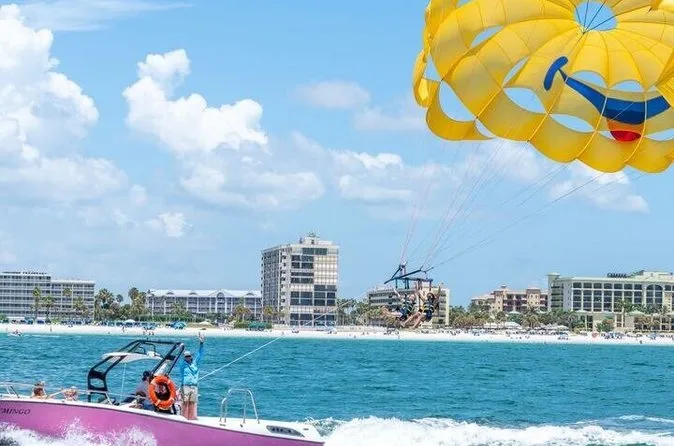A speedboat towing a parasail over the turquoise Gulf with the St. Pete Beach hotel skyline behind during parasailing on St. Pete Beach Florida