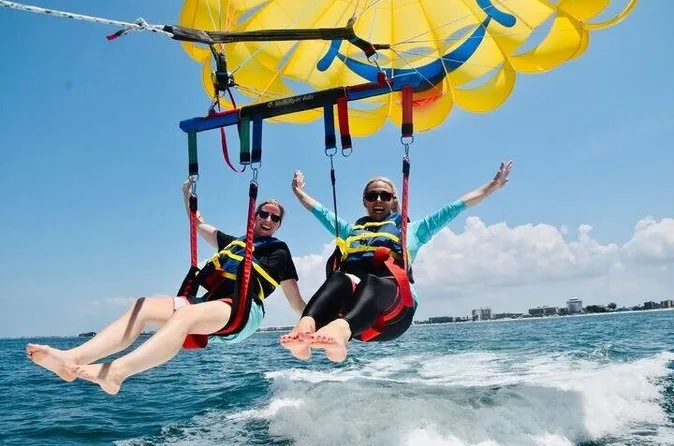 Two smiling riders in a tandem harness with their feet over the water while parasailing on St. Pete Beach Florida over the Gulf of Mexico