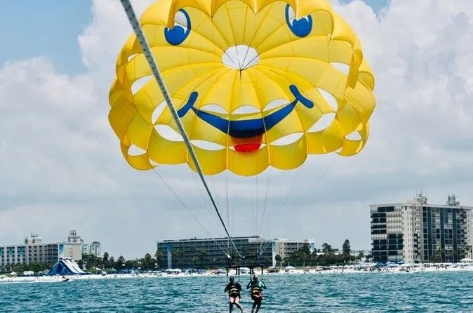 A bright smiley-face parasail canopy carrying two riders above the Gulf with St. Pete Beach behind while parasailing on St. Pete Beach Florida